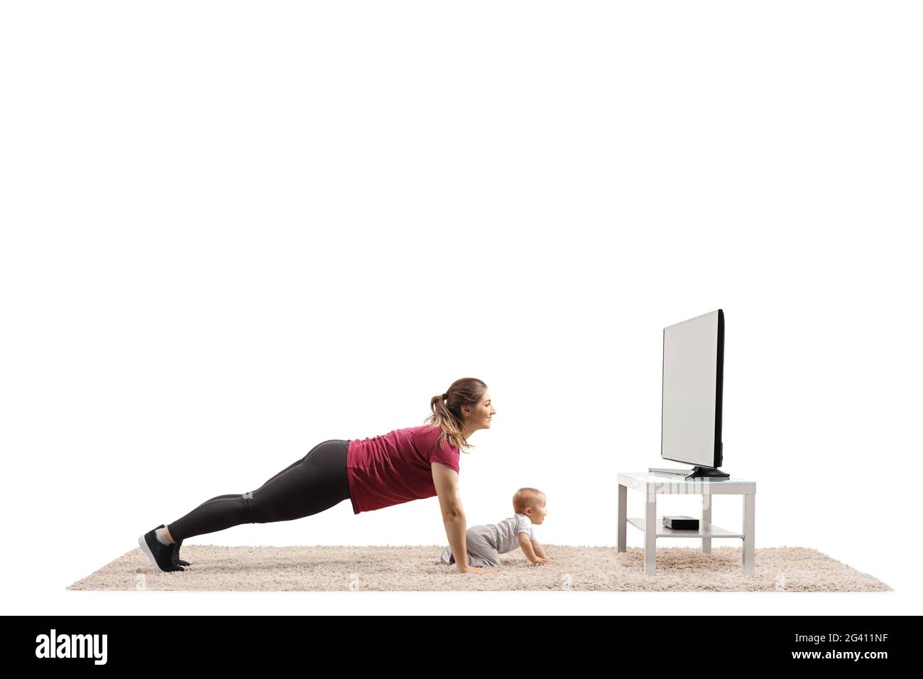 Junge Mutter macht Plankenübungen vor einem fernseher und ein Baby kriecht auf dem Teppich isoliert auf weißem Hintergrund Stockfoto