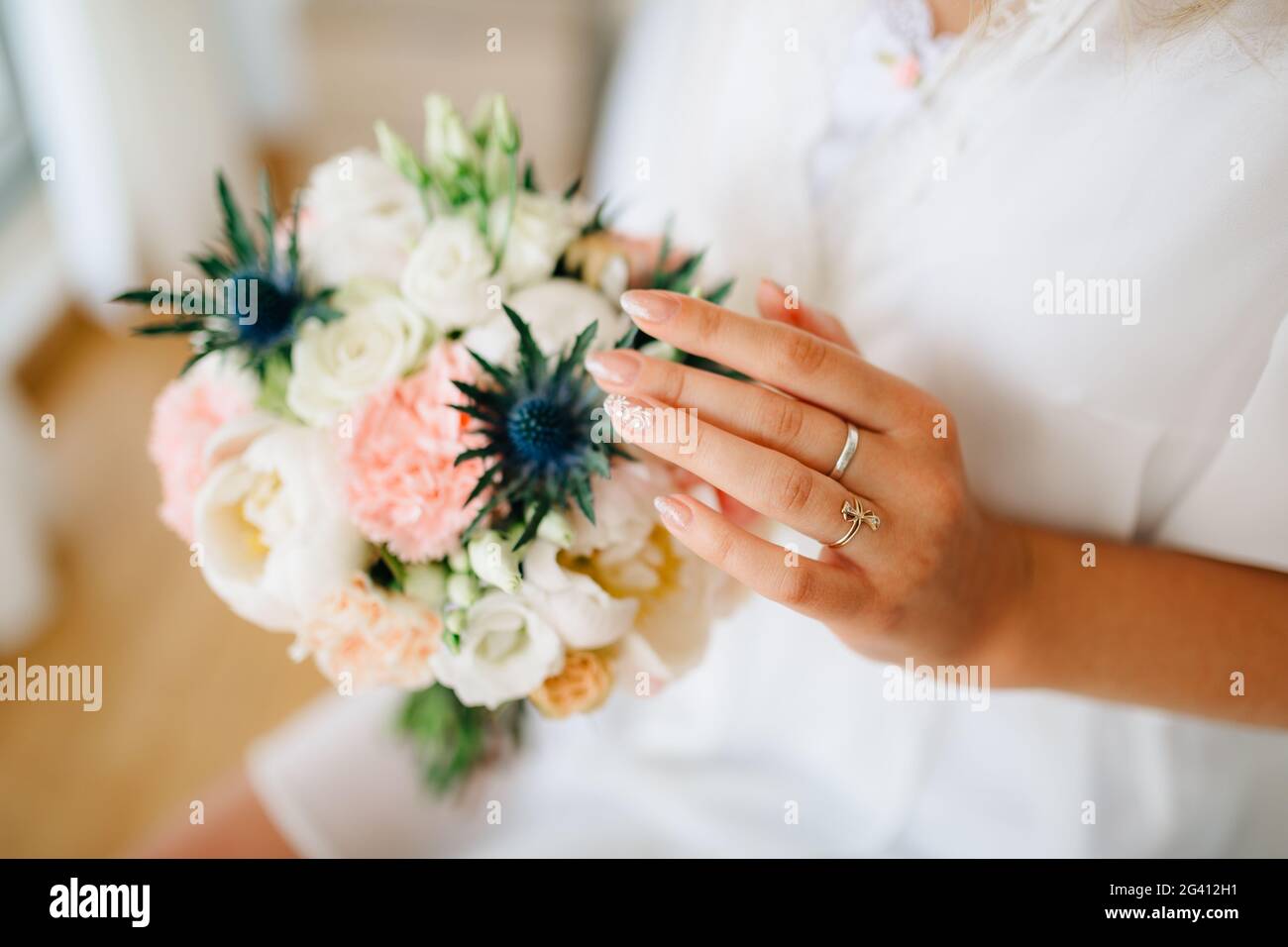 Die Braut hält sich in der Hand und berührt sanft ein Bouquet mit Pfingstrosen, Rosen, Lisianthus und Eryngien Stockfoto