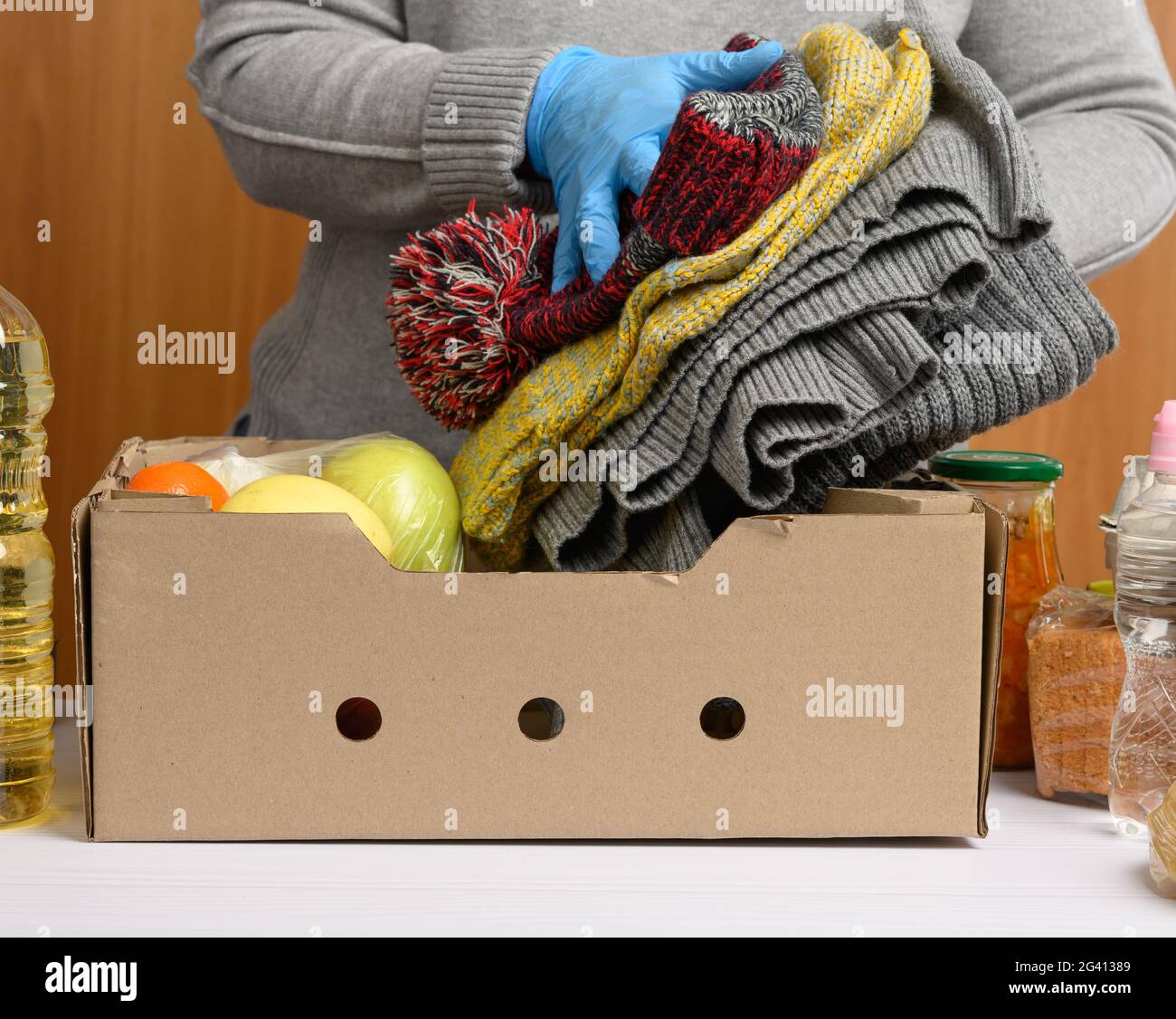 Frau in Handschuhen sammelt immer wieder Lebensmittel, Früchte und Dinge und einen Karton, um Bedürftigen zu helfen Stockfoto