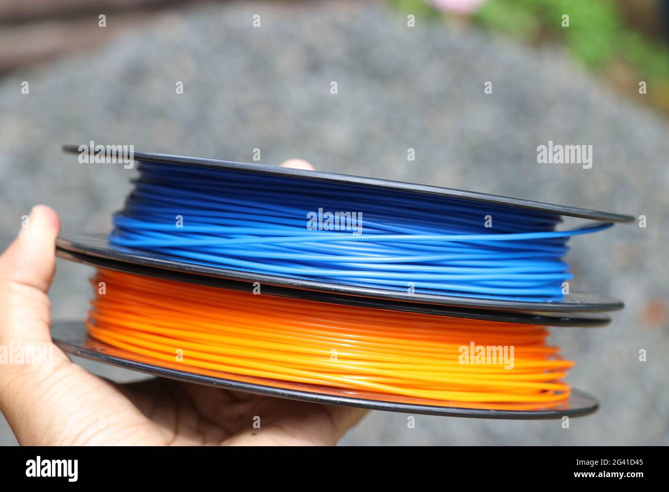 3D-Druck Filamentspulen zur Hand. Blaue und orangefarbene 3D-Drucker-Filamente für die additive Fertigung Stockfoto