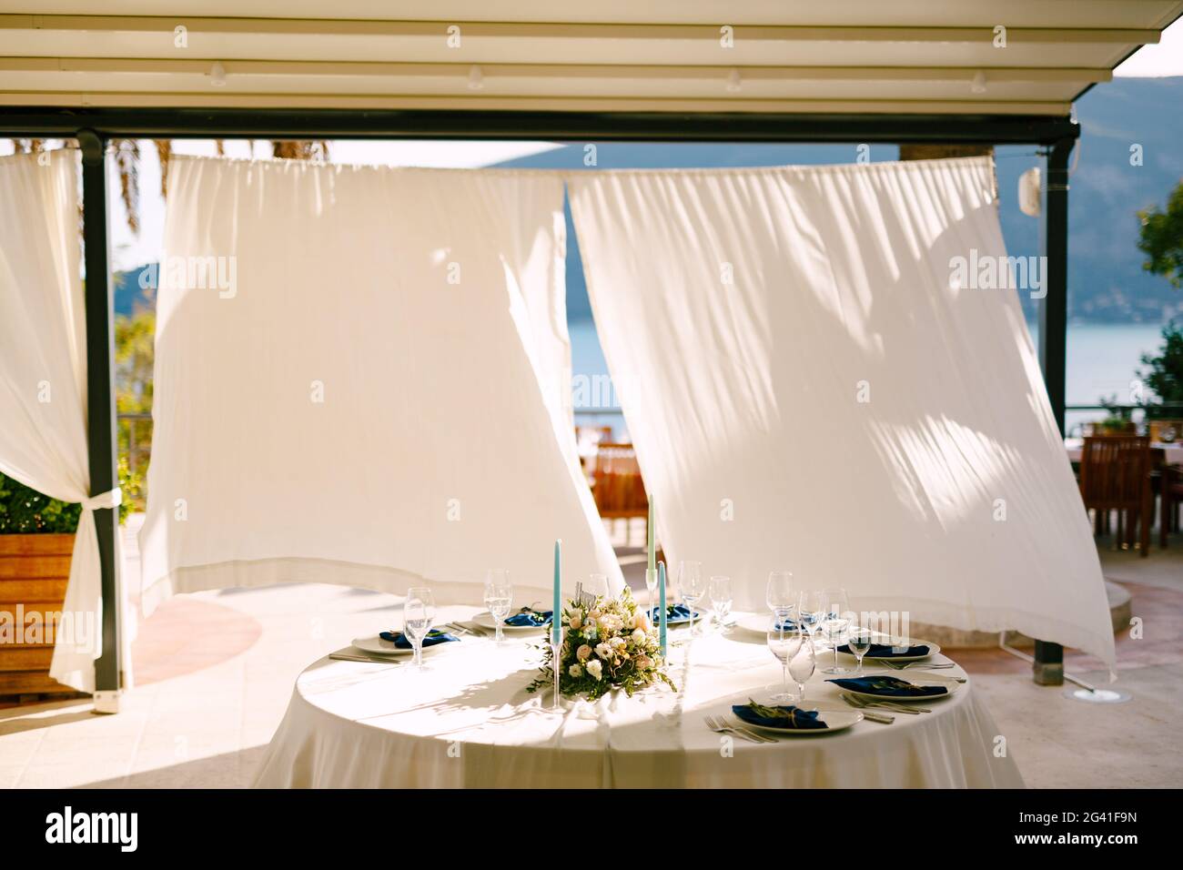 Hochzeitsessen Tischempfang. Runder Tisch mit einem Blumenstrauß in der Mitte und Kerzen, vor dem Hintergrund von Weiß Stockfoto