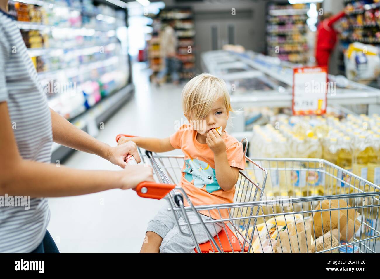 Budva, Montenegro - 17. märz 2021: Ein Kind sitzt in einem Trolley in einem Supermarkt und isst ein Brötchen. Stockfoto