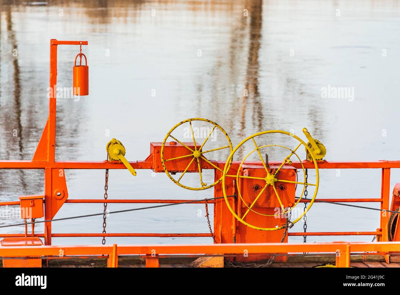 Die Details der Seilfähre, die über einen Fluss durch Kabel verbunden mit beiden Ufer. Die orange Kettenfähre, gelbes Lenkrad und blaues Wasser Stockfoto