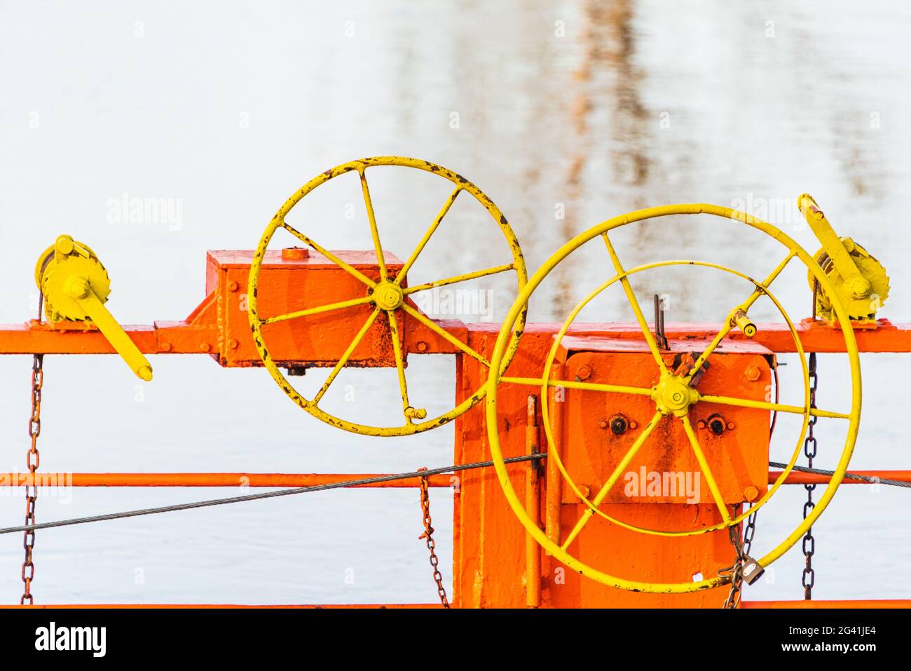 Die Details der Seilfähre, die über einen Fluss durch Kabel verbunden mit beiden Ufer. Die orange Kettenfähre, gelbes Lenkrad und blaues Wasser Stockfoto