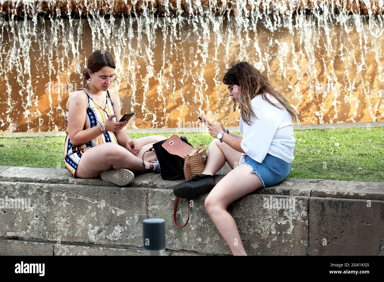 Zwei junge Frauen saßen an den Brunnen im Zentrum von Barcelona am Telefon. Stockfoto