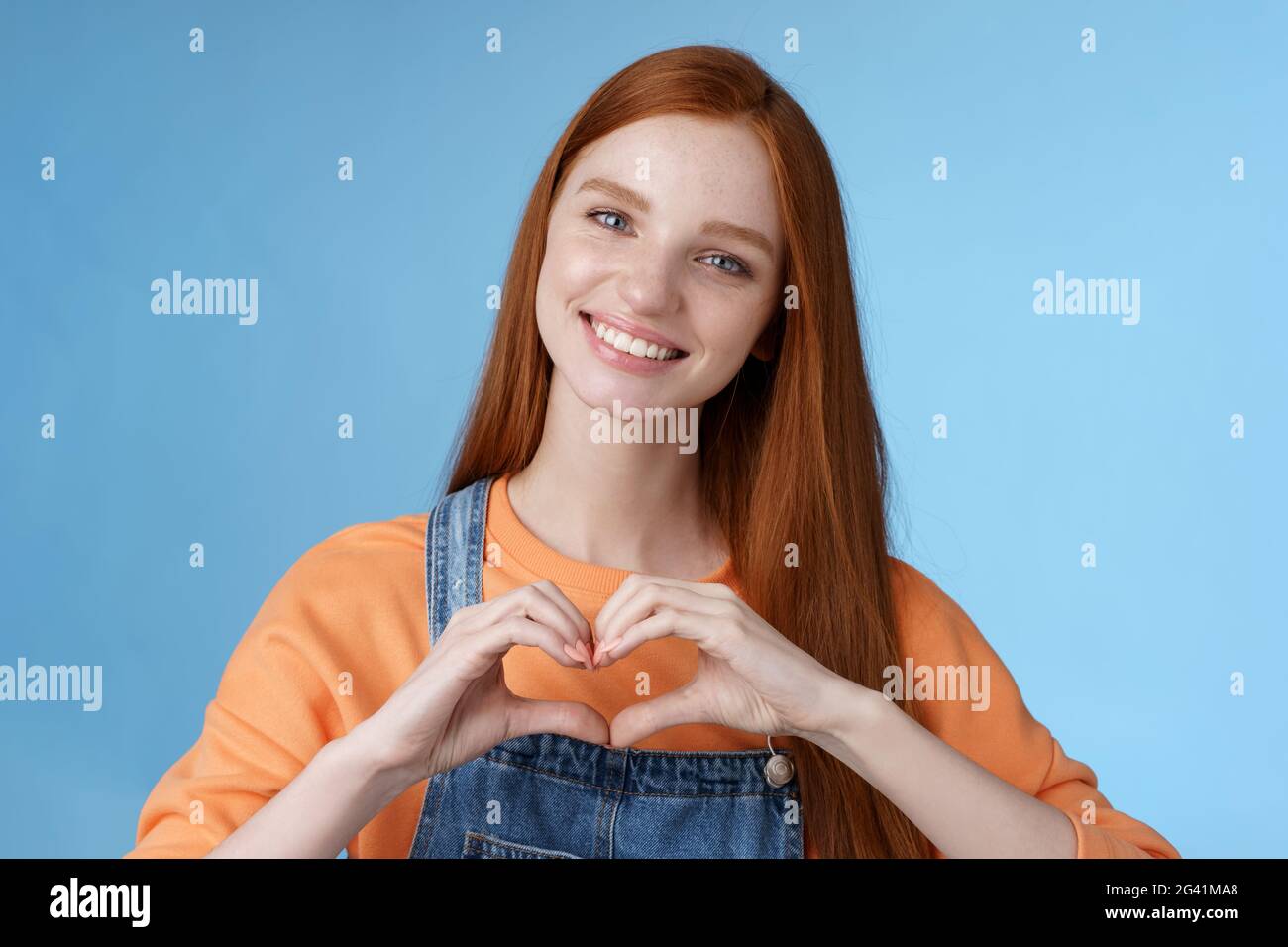 Liebe dich. Attraktive romantische zarte Rotschopf lächelnd sanfte Freundin blaue Augen Sommersprossen zeigen Herz Brust drücken Sympathie roma Stockfoto