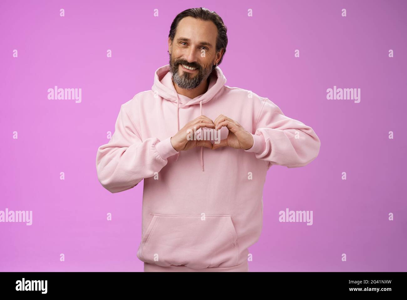 Familie im Herzen. Portrait schön schön schön romantisch bärtig Mann in rosa Kapuzenpullover leidenschaftlich aussehende Kamera zeigen Liebe Geste Smili Stockfoto