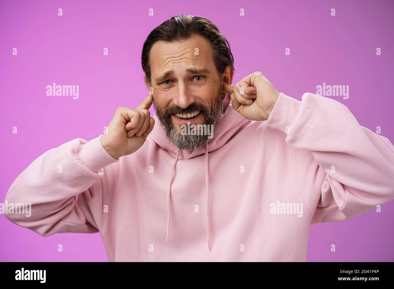 Unzufrieden genervt erwachsenen bärtigen Mann fühlen sich unwohl abgelenkt laut schrecklichen Lärm runzelig knarren hören schlechten Musiker Gitarre spielen Stockfoto