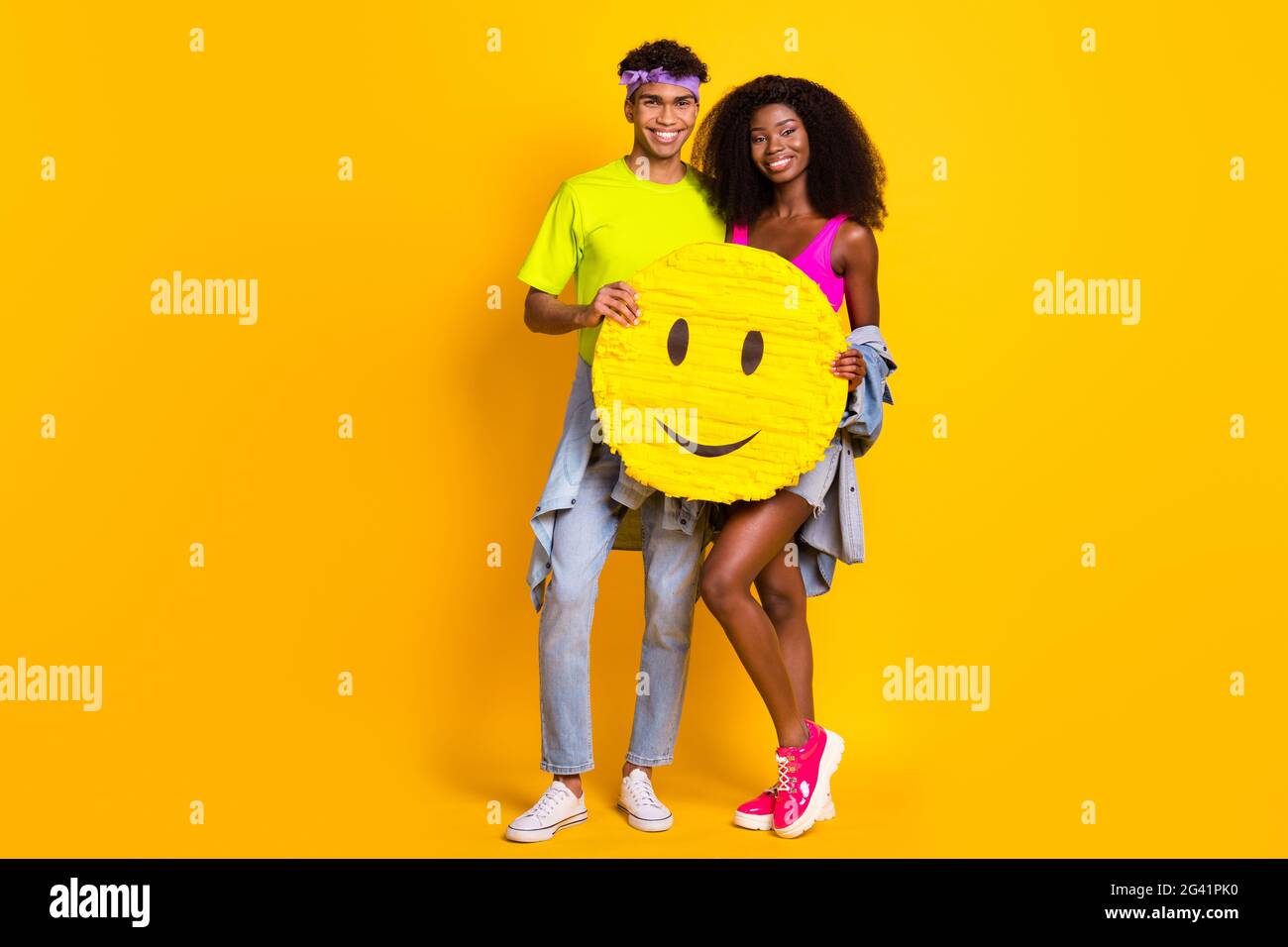 Foto von niedlichen glänzenden jungen Paar gekleidet Denim-Outfit mit riesigen Smiley-Zeichen Umarmung vereinzelte gelbe Farbe Hintergrund Stockfoto