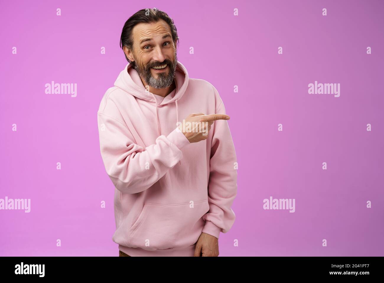 Freundlicher, sorgloser kaukasischer bärtiger Mann in pinkem Hoodie, der direkt auf Familienmitglieder hinweist, die stolz lächeln, erfreut die Show Stockfoto
