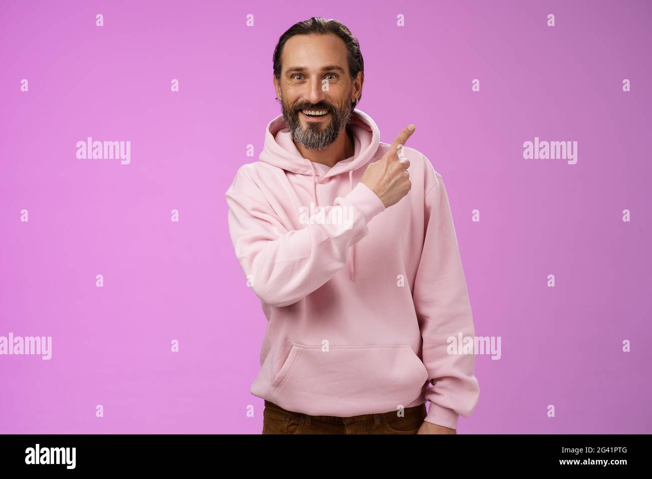 Gut aussehende glückliche, energiegeladene, glückliche, reife, graue Haare aus den 50er Jahren im trendigen Hipster-Hoodie, der in der rechten oberen Ecke auf amüsiertes Erzählen zeigt Stockfoto
