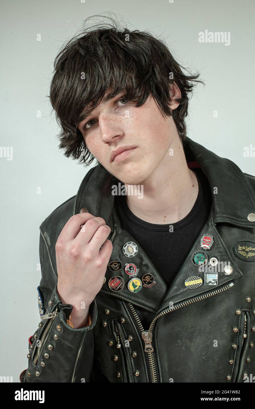 Junger Biker mit Rocker-Lederjacke, die innen mit Nieten, Aufnäher und Abzeichen mit weißem Hintergrund überzogen ist. Stockfoto