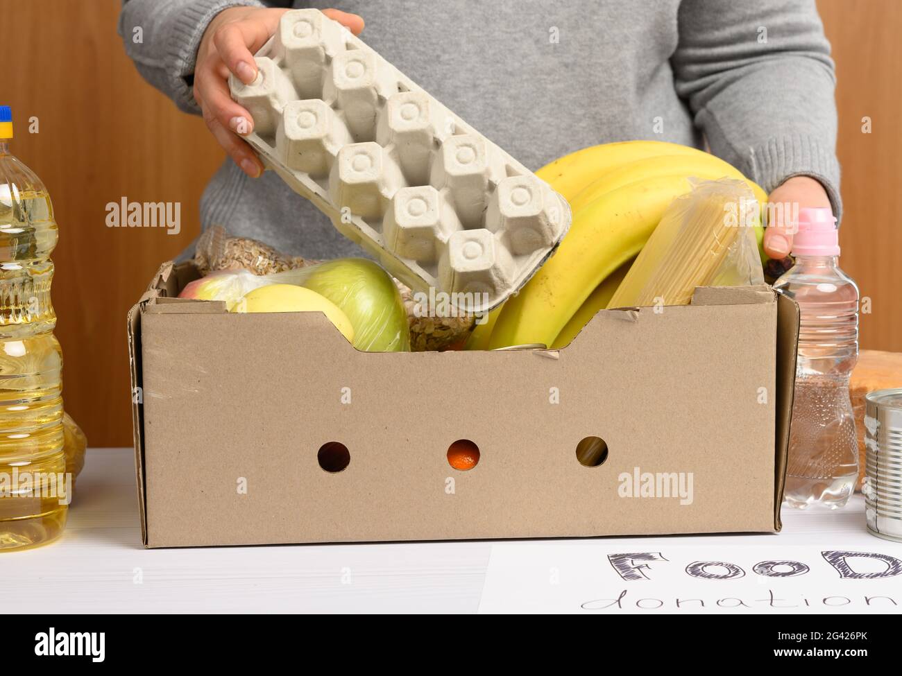 Frau in Handschuhen sammelt immer wieder Lebensmittel, Früchte und Dinge und einen Karton, um Bedürftigen zu helfen Stockfoto