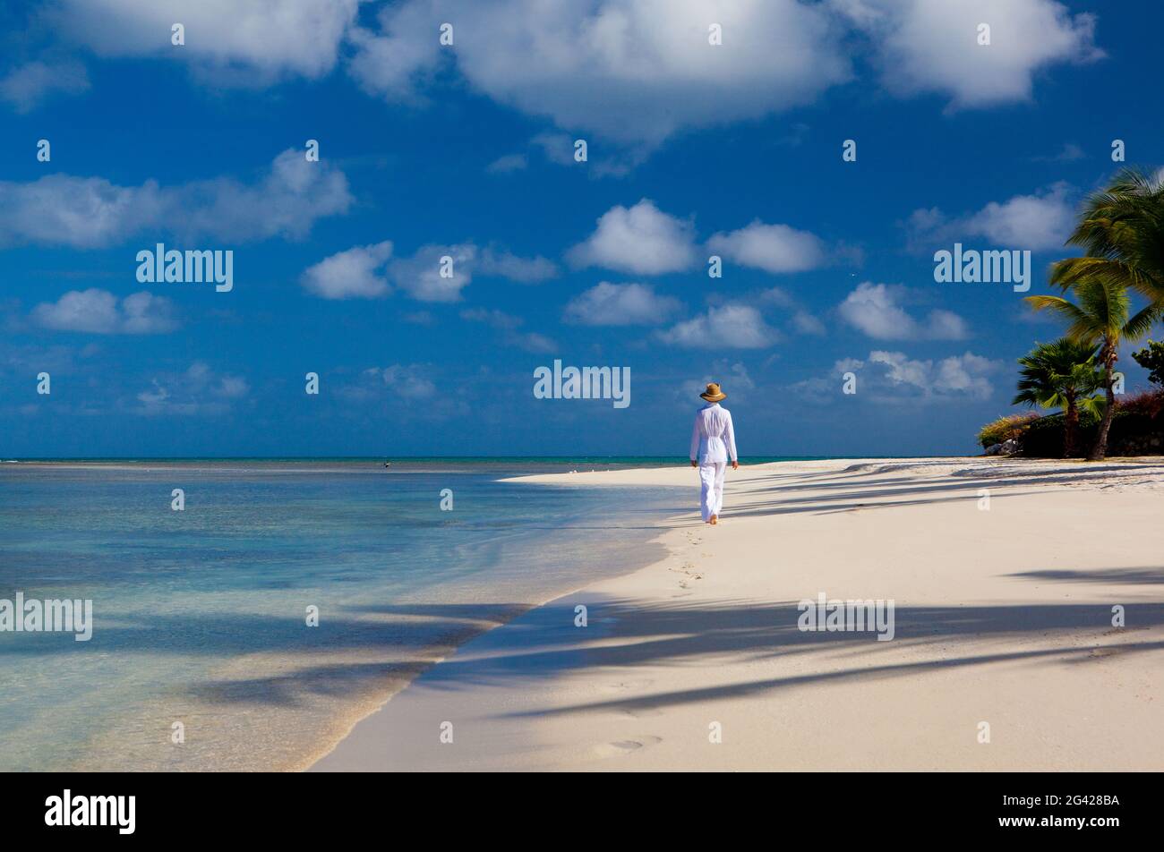 Eine Frau in weißer, tropischer Kleidung geht an einem unberührten Strand entlang. Antiugua, Westindien. Stockfoto