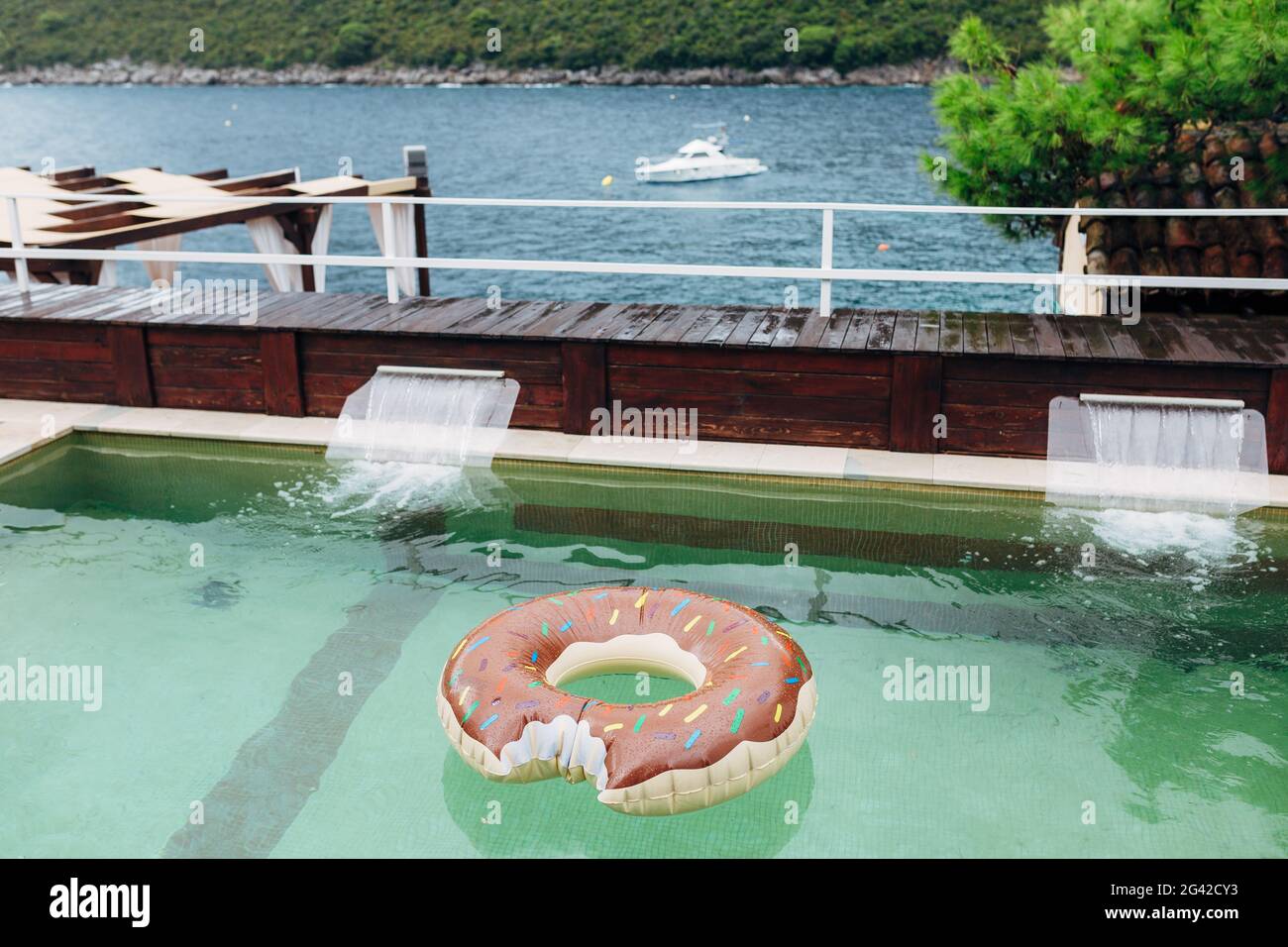 Ein schwimmender aufblasbarer Kreis schwimmt in einem Schwimmbad mit Blick auf das Meer, die Berge und eine Yacht mit Ankerblick. Stockfoto