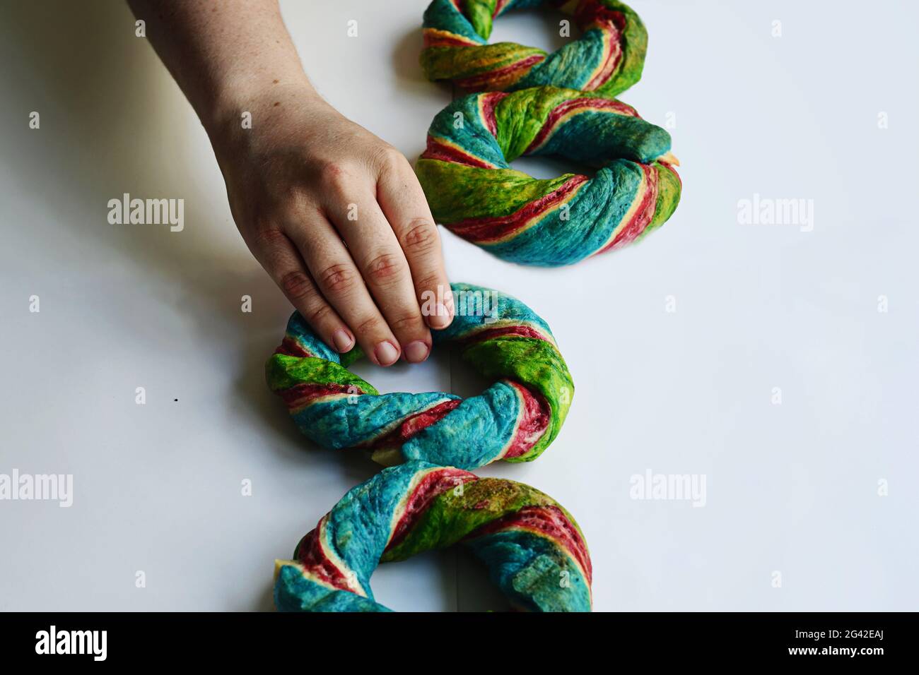 Person, die einen Regenbogen-Bagel in die Reihe der bunten Frühstück Bagels. Stockfoto