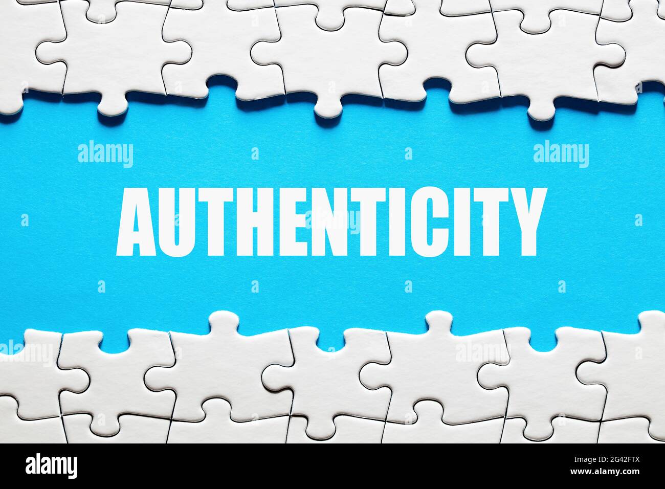 Das Wort Authentizität auf blauem Hintergrund, eingerahmt von Puzzleteilen. Die Wahrheit, Realität oder das Zuverlässigkeitskonzept zu entdecken oder zu offenbaren. Stockfoto
