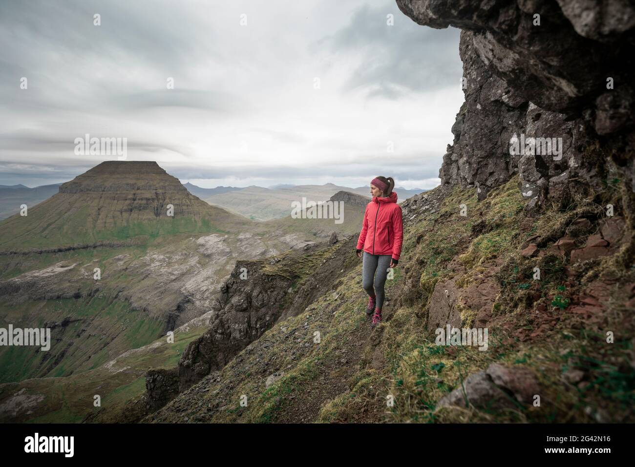 Frau, die in der Landschaft der Färöer-Inseln unter dramatischen Wolken wandert Stockfoto