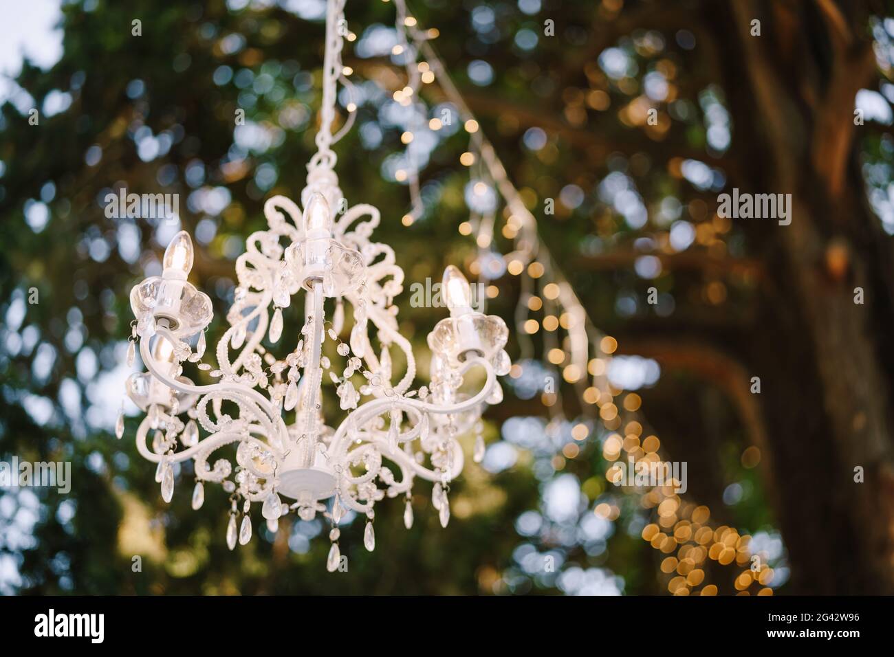 Sechs-Licht-Kristall-Kronleuchter und Girlande hängen vom Baum. Dekorieren eines Hochzeitsessers im Freien. Stockfoto