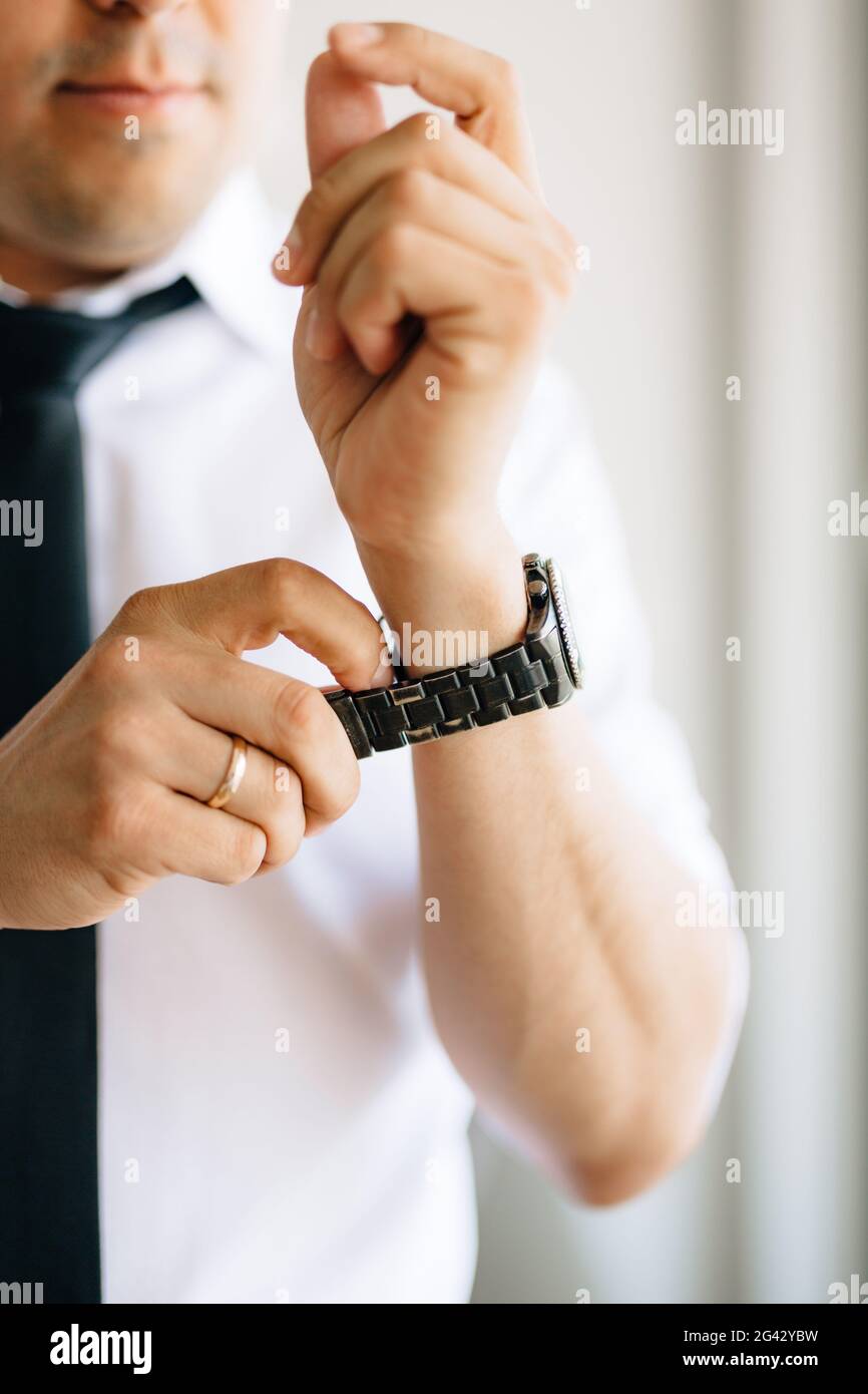 Ein Mann in einem weißen Hemd und Krawatte legt ein Beobachten Sie seine Hand während der Vorbereitung auf die Hochzeitszeremonie Stockfoto