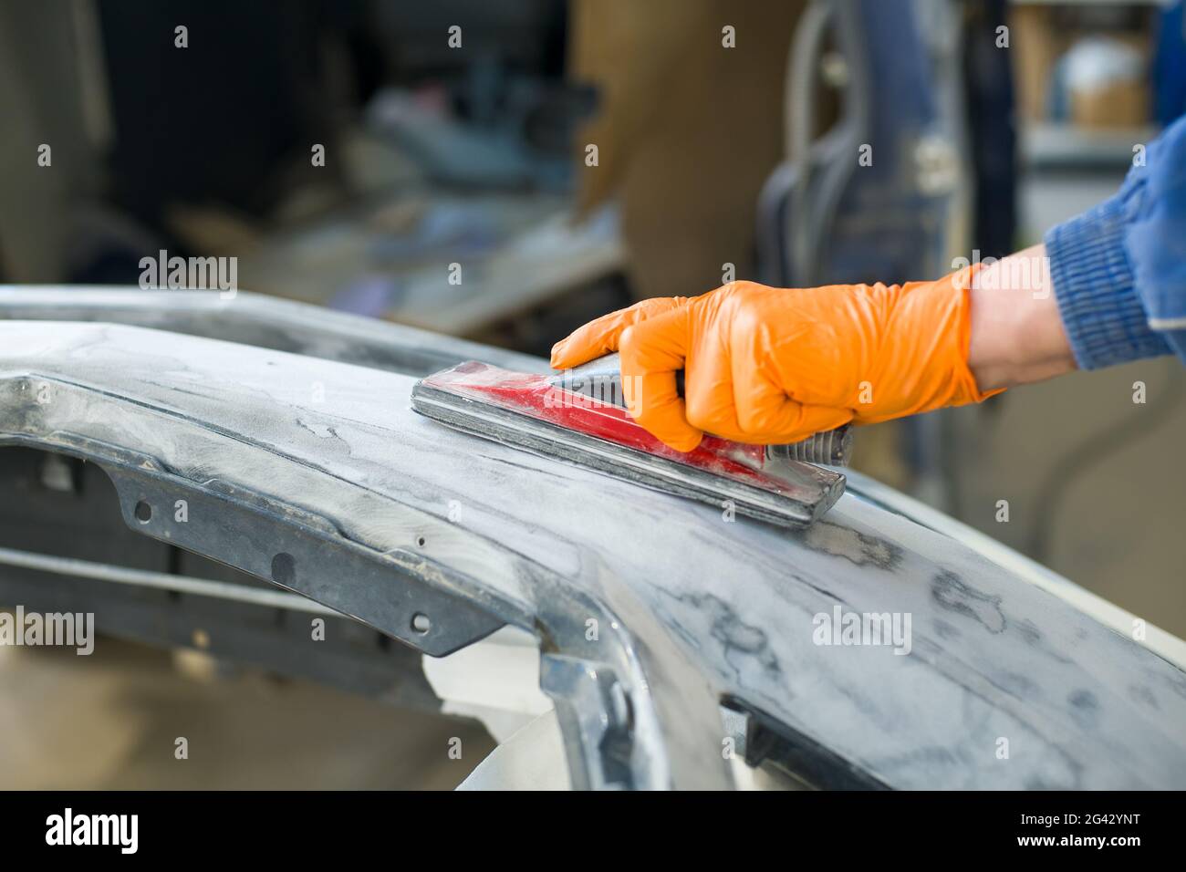 Vorbereitung zum Lackieren eines Autostoßfängers. Hand in einen Handschuh mit einem Schleifwerkzeug Stockfoto