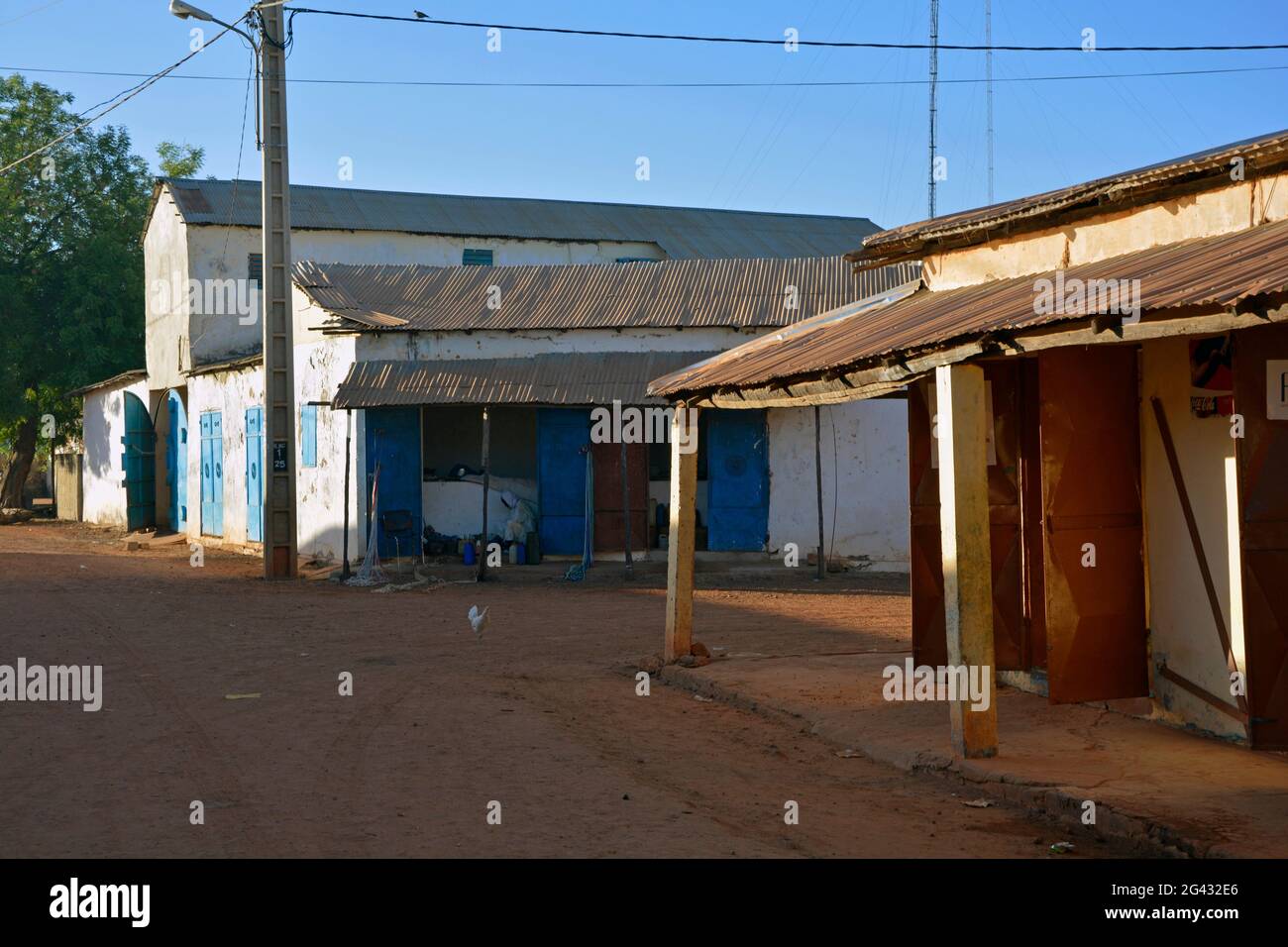 Gambia; Central River Region; Kuntaur; Hauptstraße mit Geschäften; ein Mann sitzt in seinem Laden im hinteren Gebäude; Huhn läuft auf der Straße Stockfoto