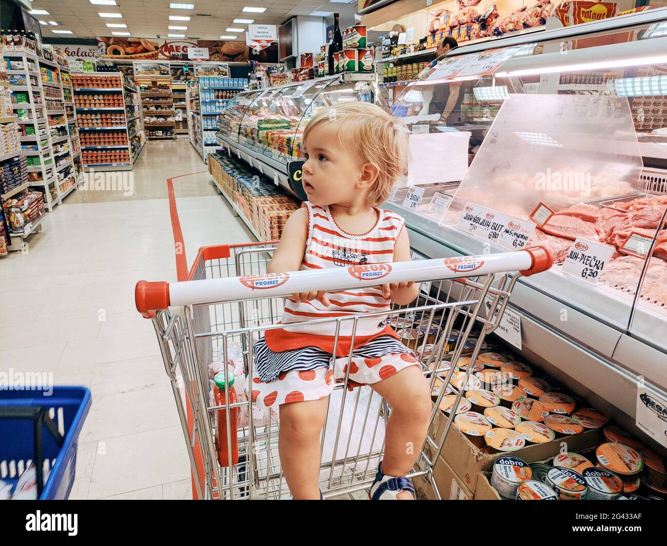 Budva, Montenegro - 10. juni 2020: Ein einjähriges Mädchen sitzt in einem Supermarkt-Trolley in der Fleischabteilung. Stockfoto