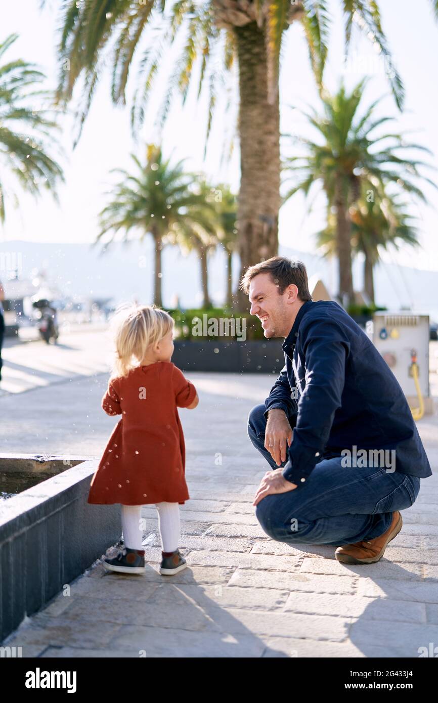 Das kleine Mädchen ist während ihres Vaters im Gesicht spritzeres Wasser Wandern auf einer Promenade Stockfoto