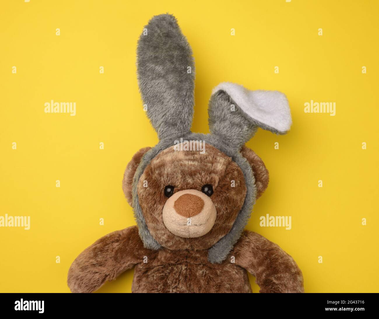 Niedlicher brauner Teddybär trägt eine Kaninchenmaske mit langen Ohren auf dem Kopf Stockfoto