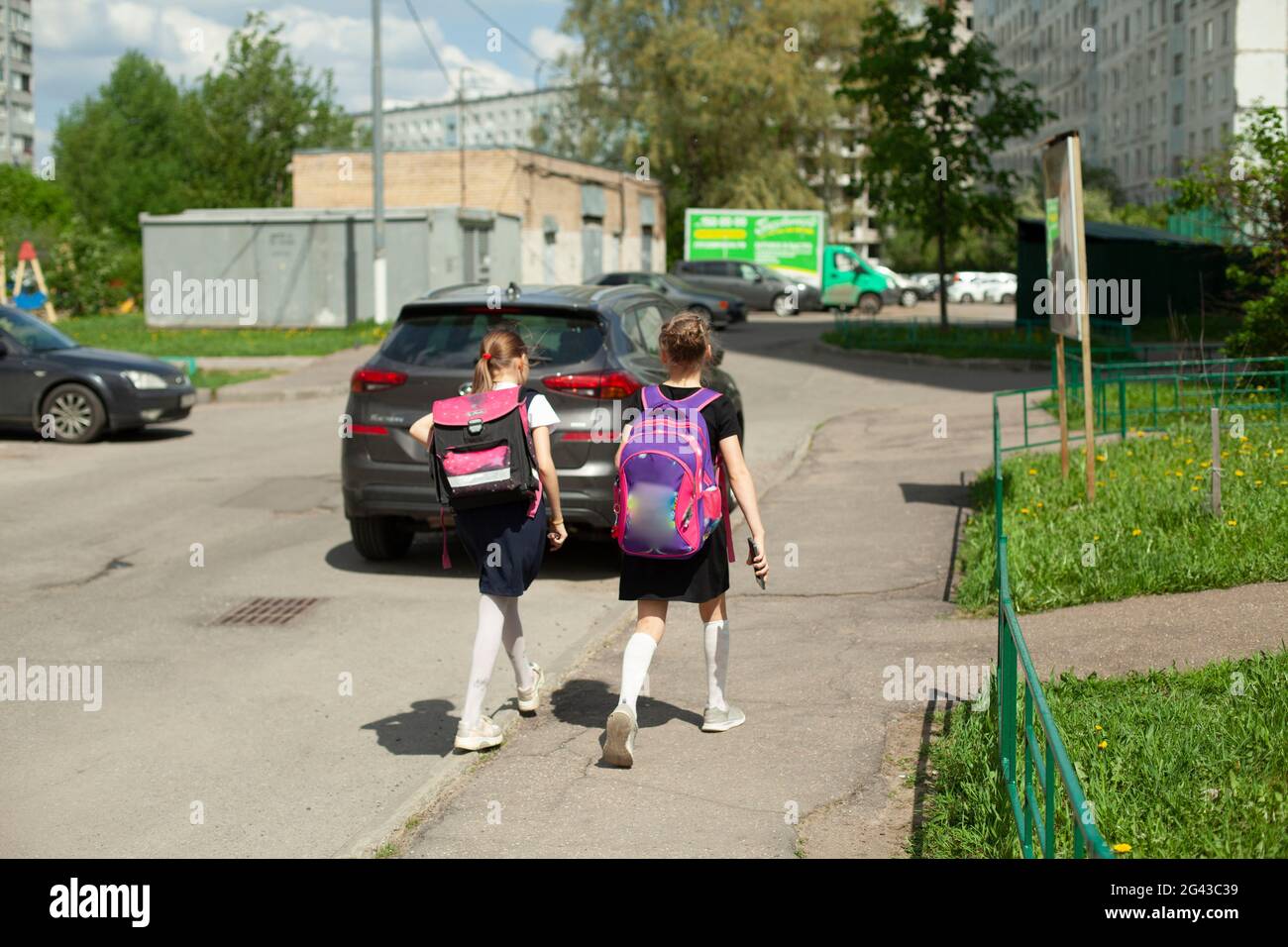Zwei Schülerinnen gehen mit Rucksäcken nach Hause. Die Mädchen gehen nach der Schule die Straße entlang. Schülerinnen in Russland. Jüngere Schülerinnen eilen zur Schule. Stockfoto