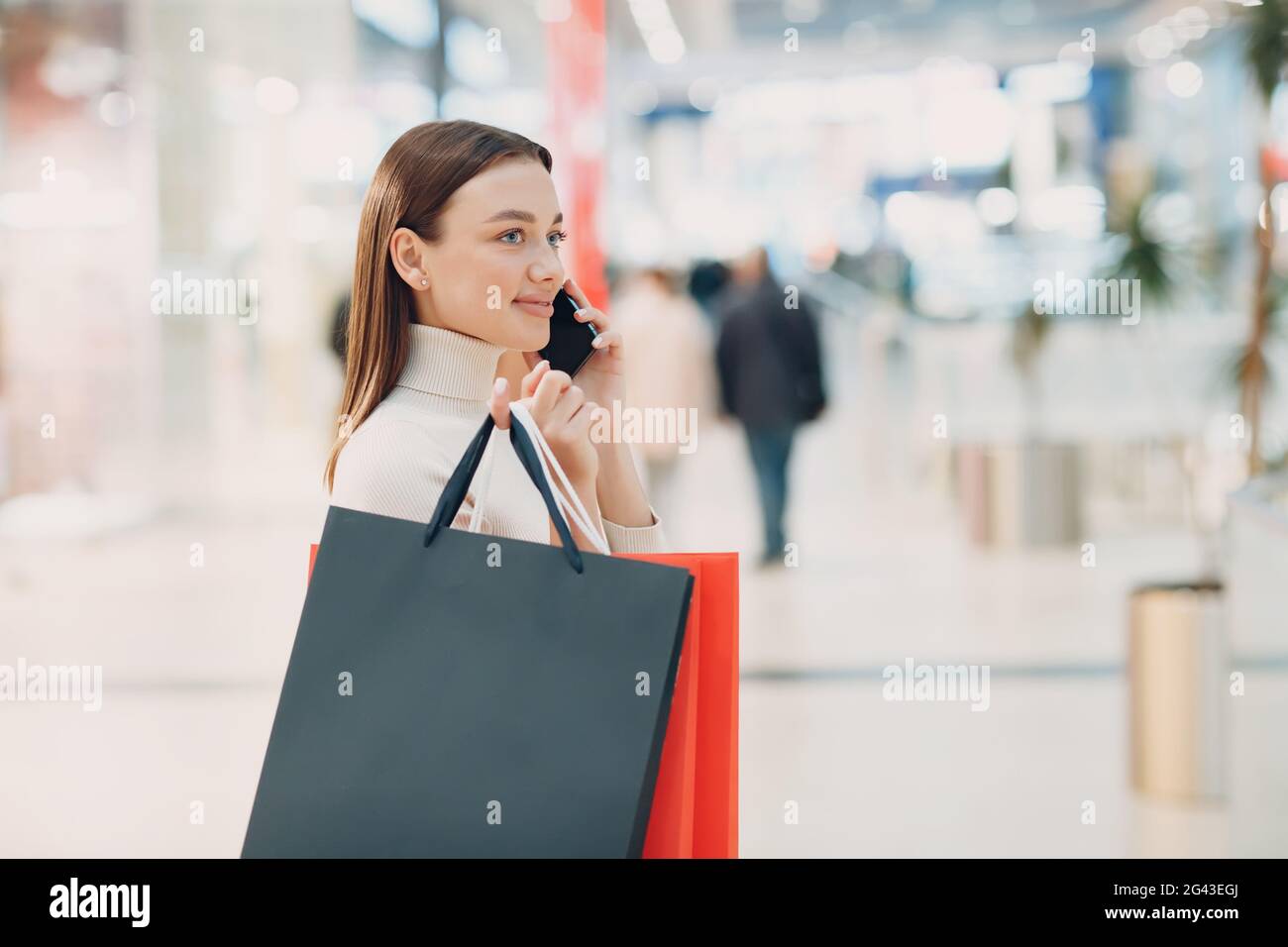 Positive junge Erwachsene Frau, die Einkaufstaschen aus Papier und Mobiltelefon in den Händen trägt Stockfoto