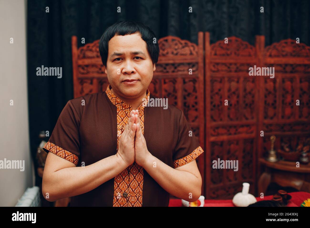 Thailändischer Mann lächelt Porträt mit traditionellen Thai Anzug und willkommen beten Geste gefaltet Hände Stockfoto
