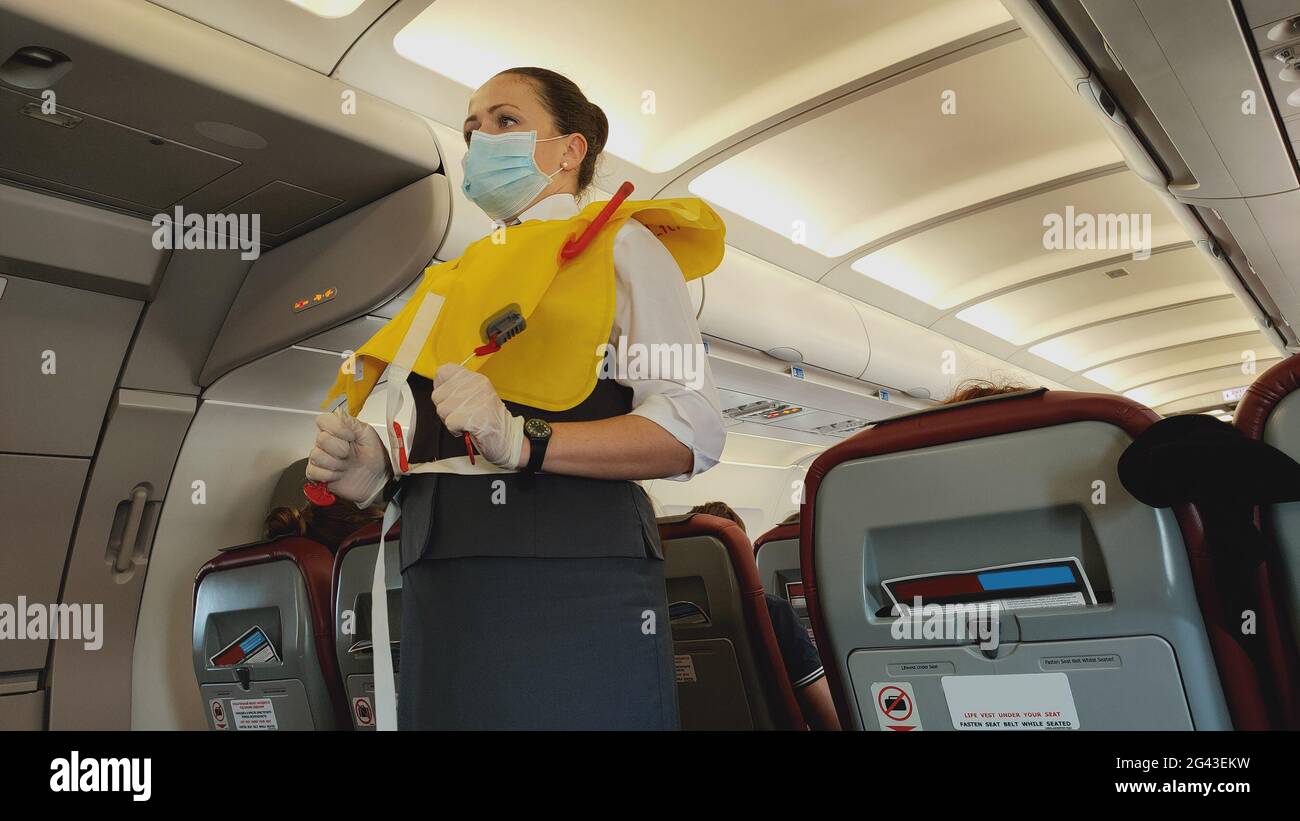 Eine Stewardess-Flugbegleiterin in Gesichtsmaske, die vor dem Abflug eine Schwimmweste an Bord vorstellt Stockfoto