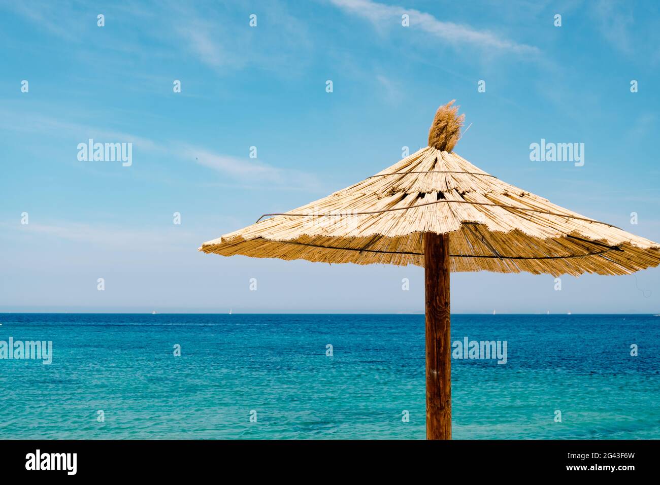 Ein Strand mit Strohschirm gegen den blauen Himmel und azurblauem Wasser an einem Sandstrand in Kroatien, in der Stadt Primosten. Stockfoto