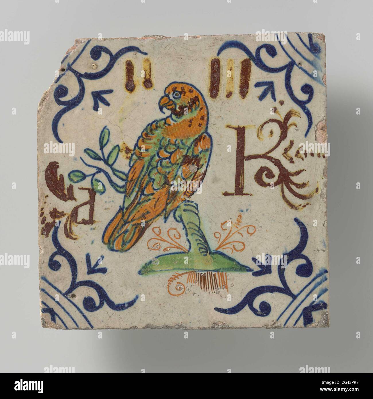 Fliesen mit Papagei. Fliesen mit einem mehrfarbigen (blau, grün, gelb, orange und braun rot) Papagei auf einem Zweig gemalt. Auf beiden Seiten die Buchstaben P und K (?). In den Ecken ein Ochsenkopf. Stockfoto