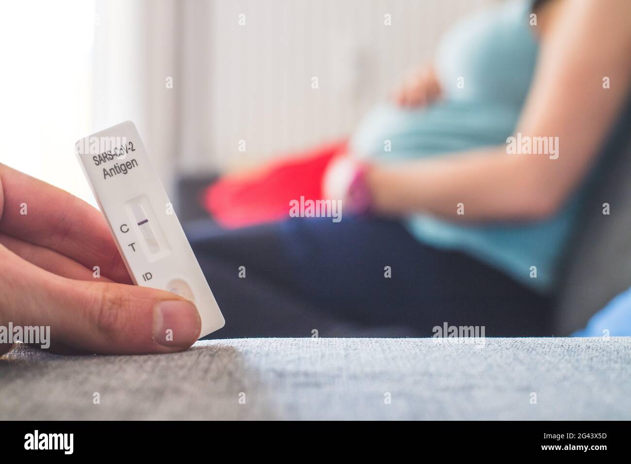 Coronavirus und Covid19 während der Schwangerschaft: Nahaufnahme der Finger, die einen negativen Covid-Antigen-Test halten, Schwangere im Blurr Stockfoto