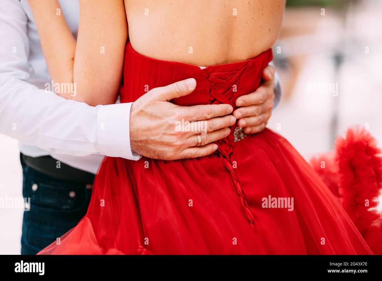 Die Hände des Mannes umarmen die Taille einer Frau in einem roten gekleidet Kleid Stockfoto