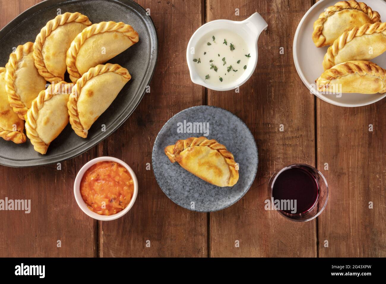 Empanadas mit Saucen und Wein, von oben auf dunklem Holzgrund geschossen Stockfoto