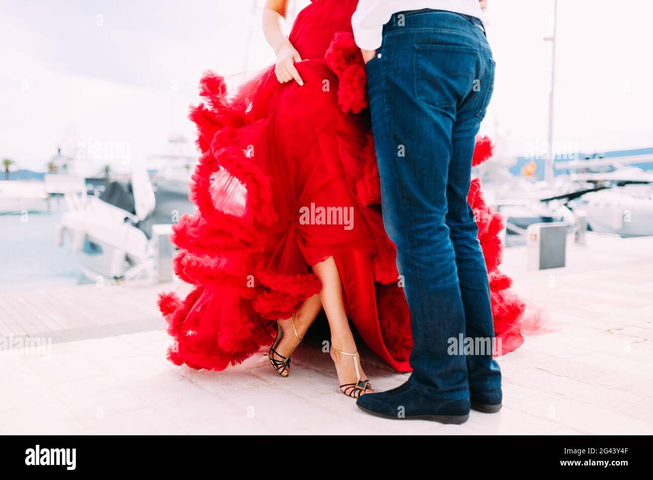 Mann, der vor einer Frau in einem roten steht Kleid auf einem Bootssteg in Montenegro Stockfoto