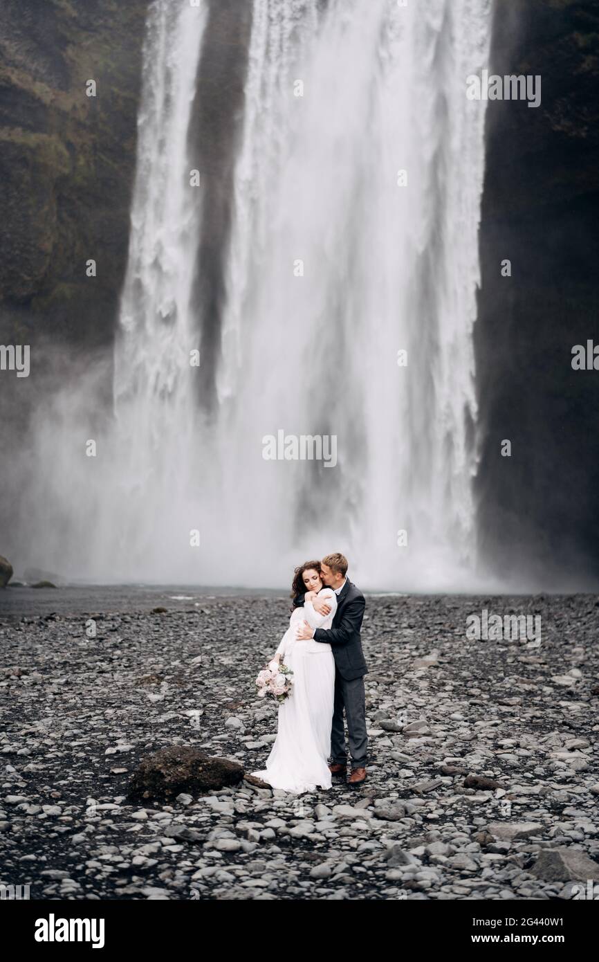 Der Bräutigam umarmt die Braut von hinten. Hochzeitspaar in der Nähe des Skogafoss Wasserfalls. Hochzeit in Island. Stockfoto