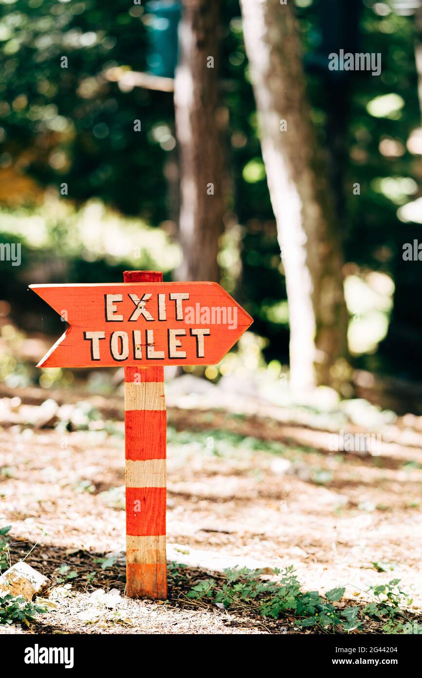 Auf dem Rasen im Wald steht ein roter Wegweiser mit einer Inschrift auf einer weiß gestreiften Säule. Titel: Ausgang Toilette Stockfoto