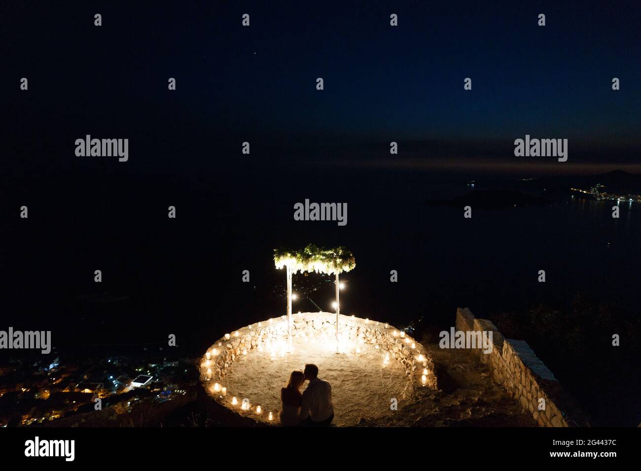 Silhouetten der Braut und des Bräutigams, die sich in der Nähe umarmen Der beleuchtete Bereich und der Hochzeitbogen am Meer Nachts Stockfoto