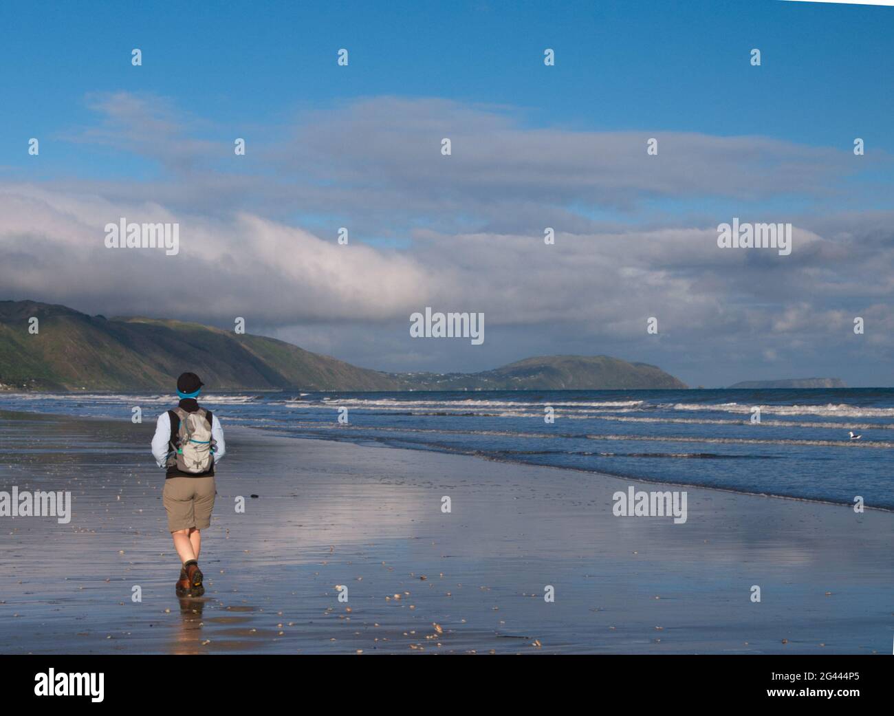 Eine Frau mittleren Alters (62) in Wanderausrüstung, die am Raumati Beach, Neuseeland, spazieren geht Stockfoto