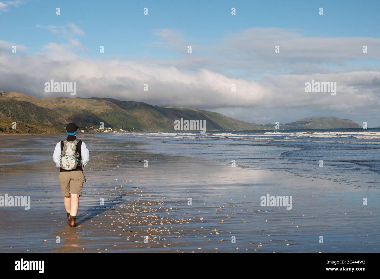 Eine Frau mittleren Alters (62) in Wanderausrüstung, die am Raumati Beach, Neuseeland, spazieren geht Stockfoto