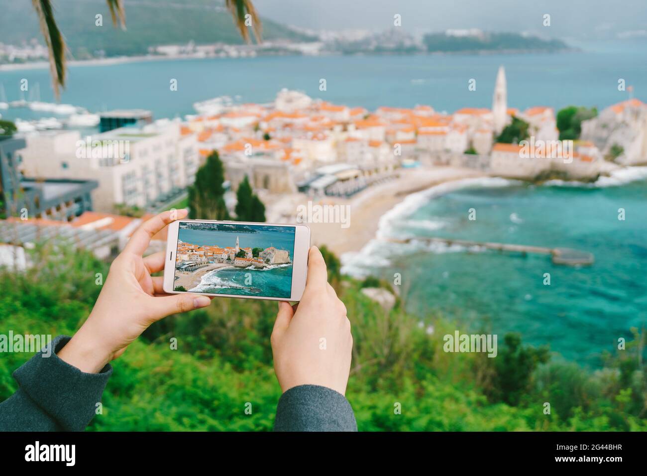 Smartphone in den Händen mit einem Foto der Altstadt Auf dem Hintergrund von Budva Stockfoto