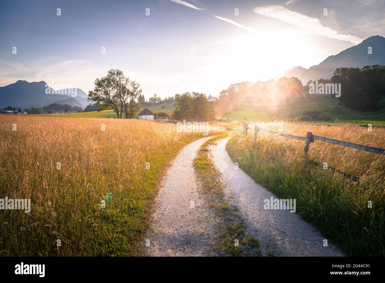 Landschaftlich schöner Sonnenuntergang: Landstraße, goldene Wiese, Hügel und Berge. Stockfoto