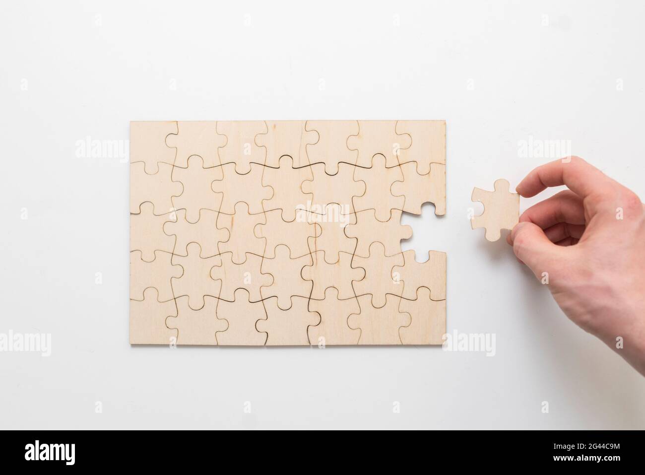 Hand hält ein Puzzleteil und komplettes Puzzle auf dem Tisch Stockfoto