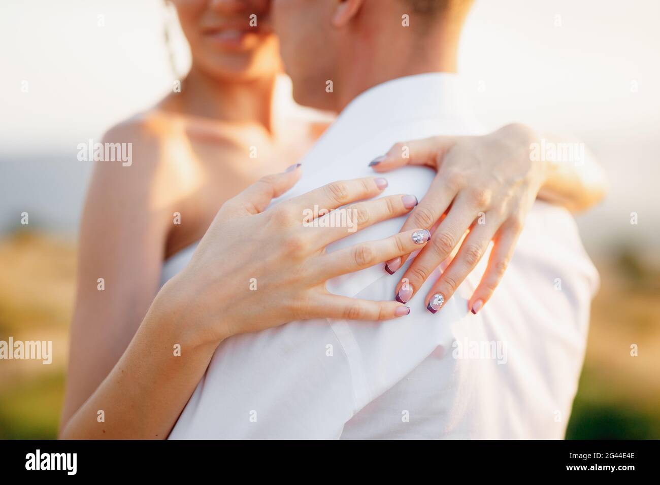Die Braut und der Bräutigam umarmen sich, die Braut legte ihre Hände auf den Rücken des Bräutigams, Nahaufnahme Stockfoto