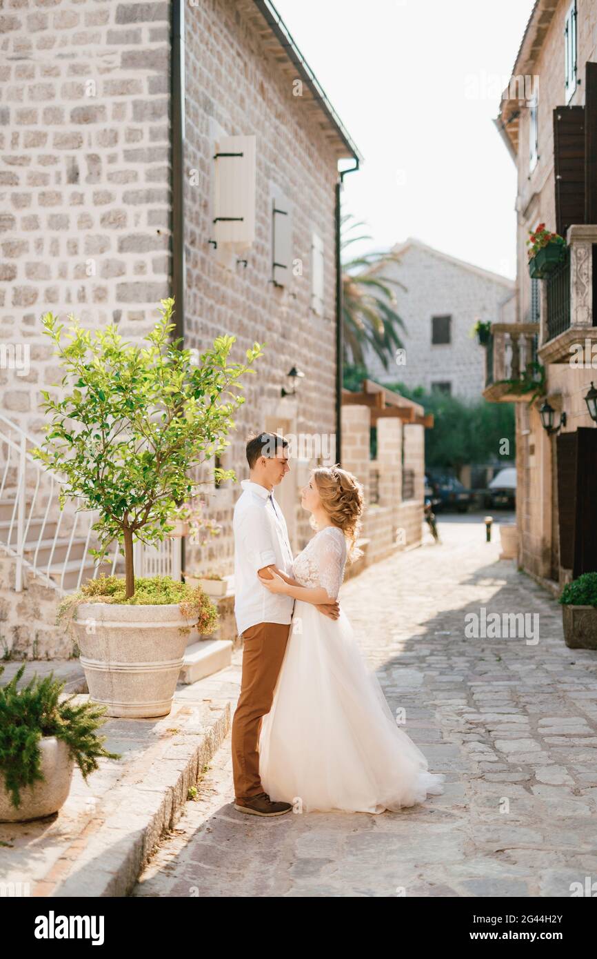 Die Braut und der Bräutigam umarmen sich in einer malerischen gemütlichen Straße Der Altstadt von Perast in der Nähe eines jungen Baumes Stockfoto