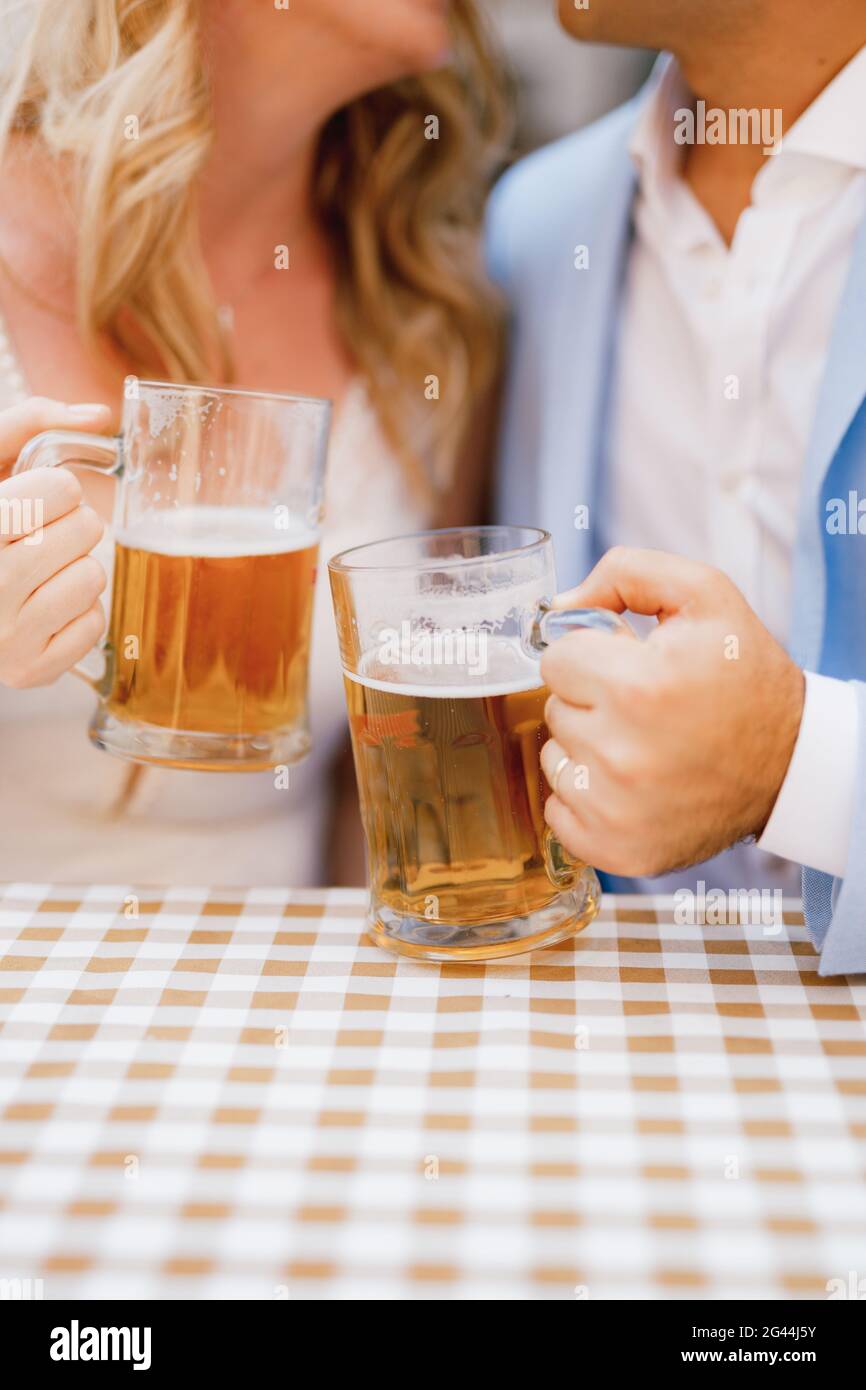 Ein Mann und eine Frau sitzen und umarmen sich Am Tisch und mit Bierkrügen Hände Stockfoto
